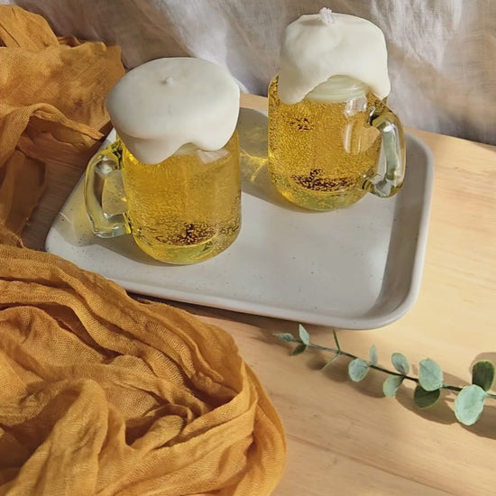 two beer candles in mini mason jars by Candle Tales. 1  is being lit, and the other is sitting in the tray next to the lit one. It's a care guide for customers.