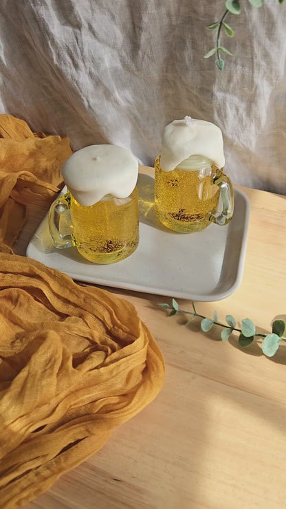 two beer candles in mini mason jars by Candle Tales. 1  is being lit, and the other is sitting in the tray next to the lit one. It's a care guide for customers.