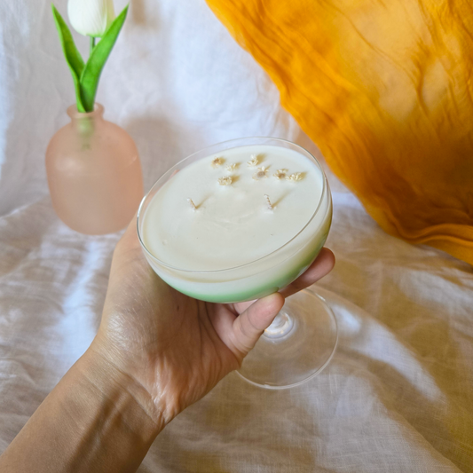 Hand holding a glass of spring fizz cocktail candle with a white tulip in the background