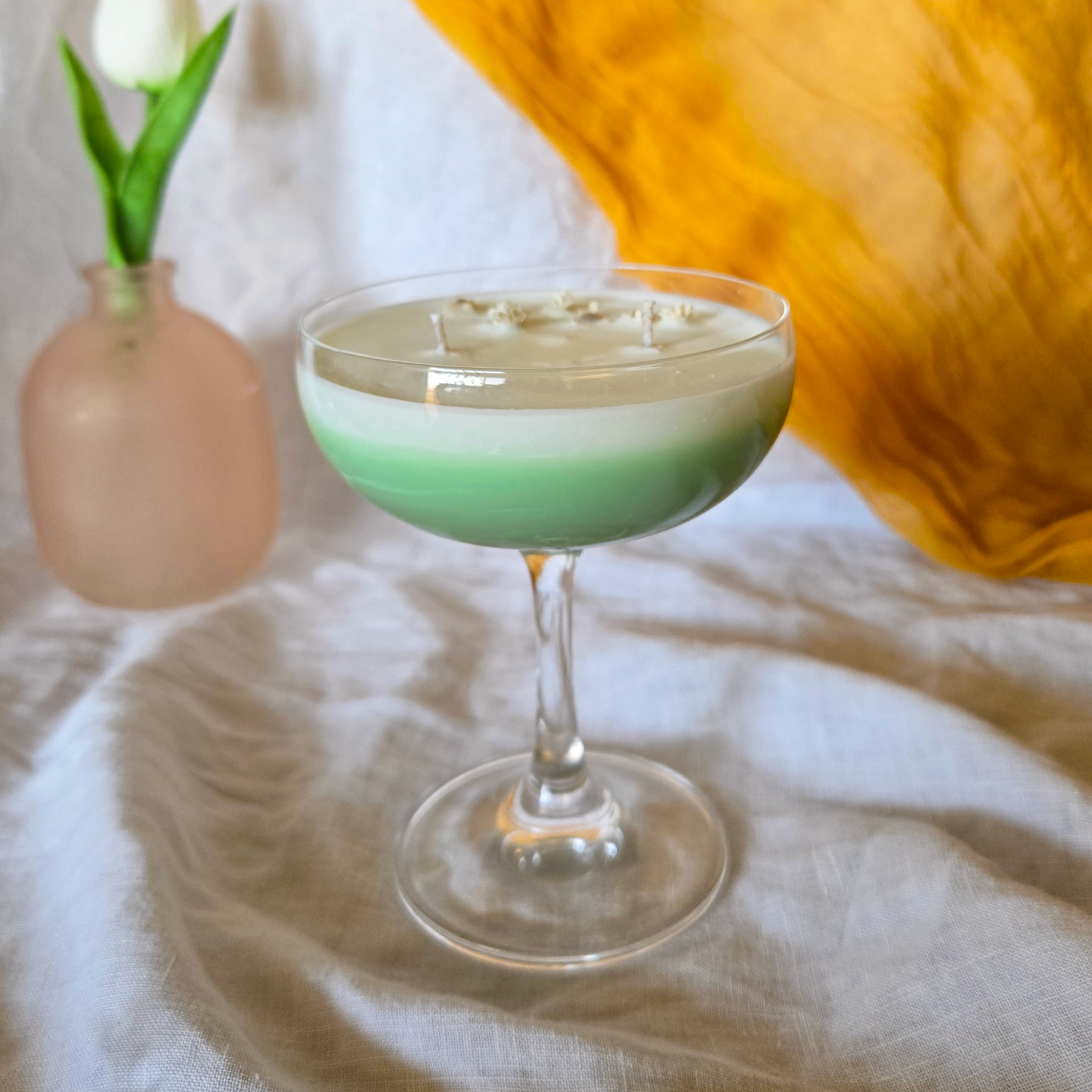 Spring fizz cocktail candle made of soy wax and dried flowers in a martini glass with a white tulip in the background