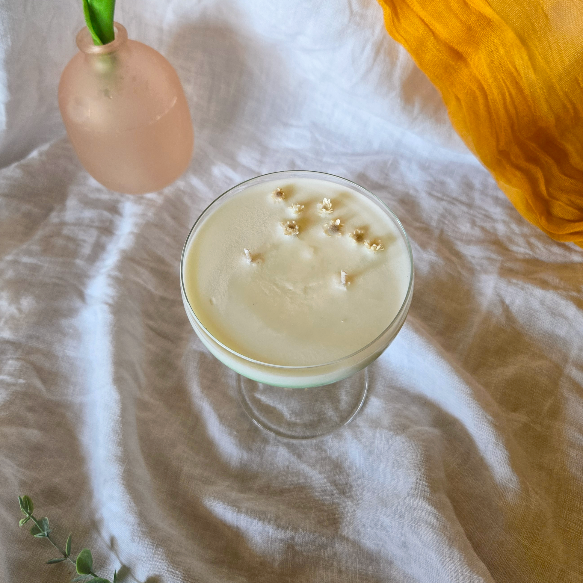a spring Cocktail candle in a martini glass with gold sprinkles on a textured white surface