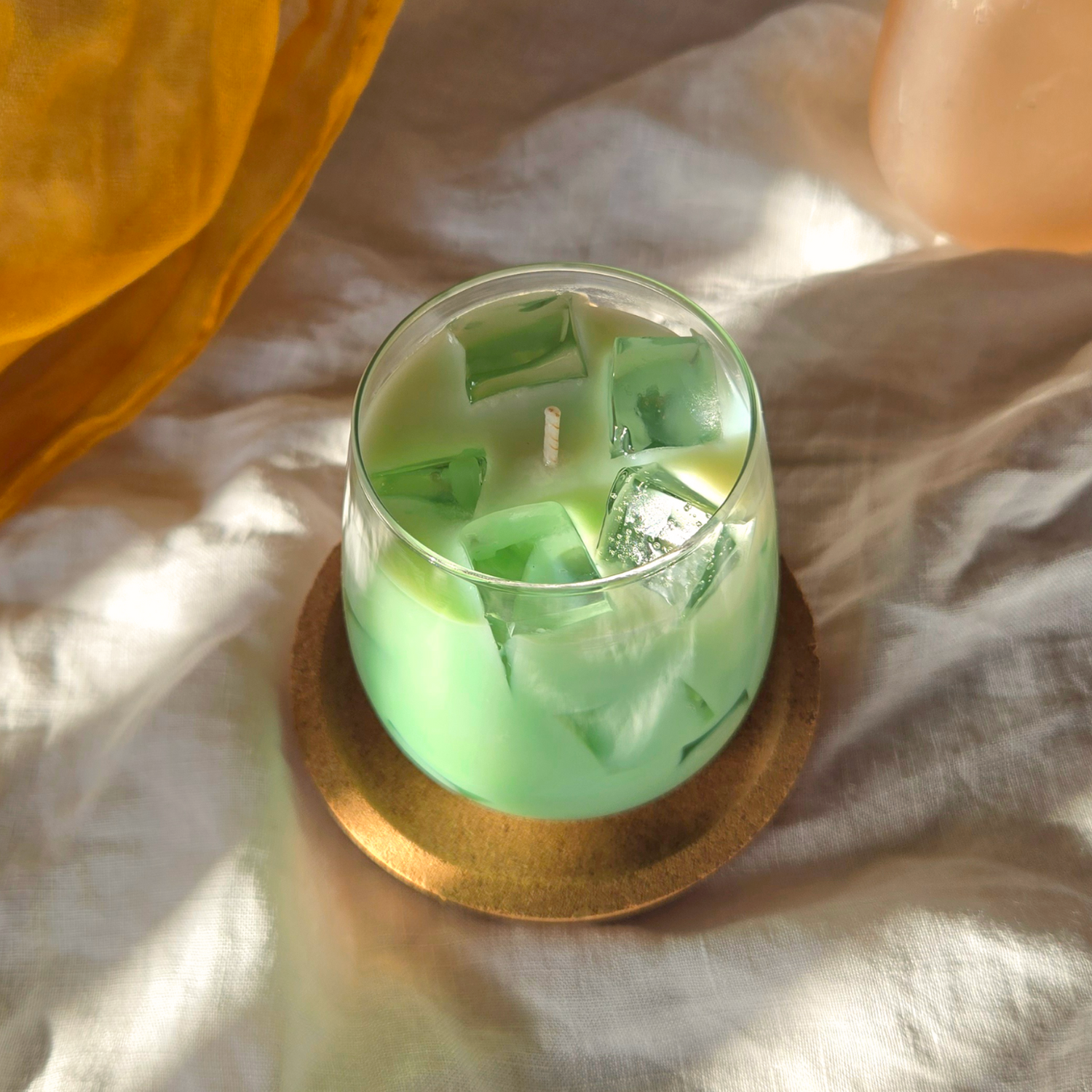 Iced match candle in a glass container on a cork coaster with an orange fabric background